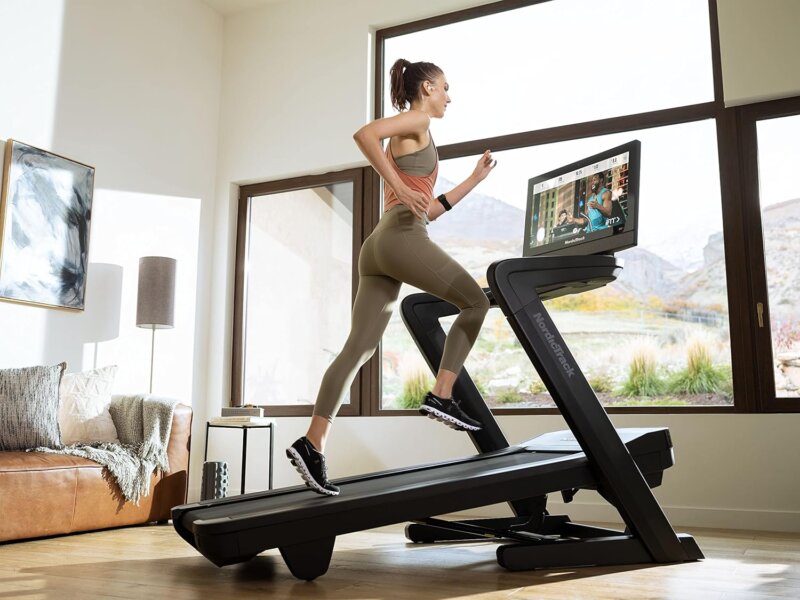 Modern treadmill with 22" Tilt and Pivot HD Screen-. User running while watching on screen coaching. the Treadmill is placed in a well lite area, with a large window to enhance workout. The Best Treadmills for Running and Walking 
