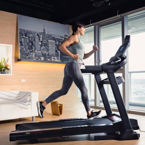 Modern treadmill with 6.5inch LCD screen. User running while watching on screen coaching. the Treadmill is placed in a well lite area, with a large window to enhance workout. The Best Treadmills for Running and Walking 